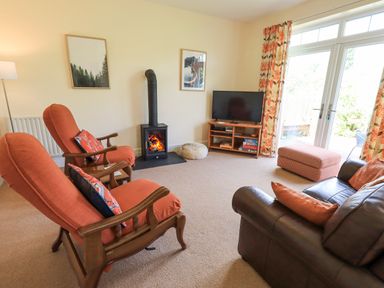 A living room with orange armchairs a leather sofa a wood stove and a television at Limhus Cottage in Keswick
