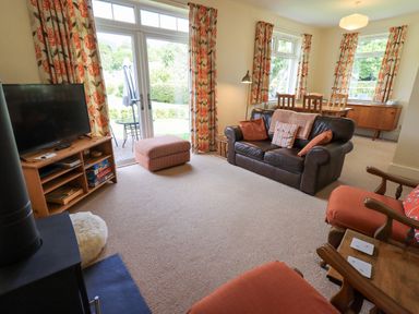 A living room with a leather sofa orange armchairs a TV on a wooden stand and a dining table with chairs at Limhus Cottage Keswick