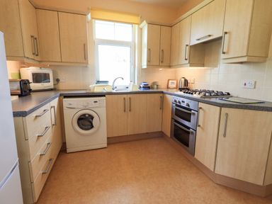 A kitchen with wooden cabinets a washing machine a gas stove and oven a toaster and a microwave at Limhus Cottage Keswick