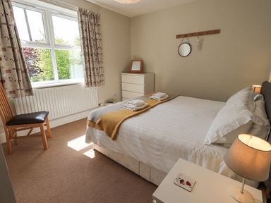 A bedroom with a bed a chair a chest of drawers and a window with curtains at Limhus Cottage in Keswick