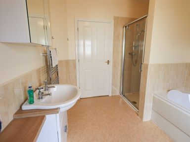A bathroom with a sink a bathtub a glass shower door and a white door at Limhus Cottage Keswick