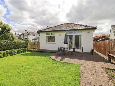 A backyard with a lawn patio table chairs and umbrella next to a white house with glass doors at Limhus Cottage Keswick