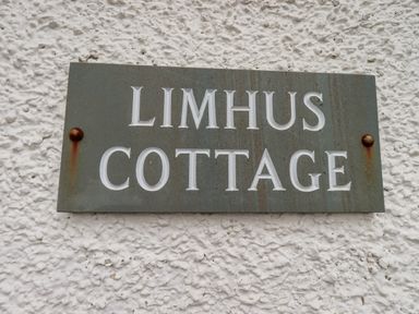 A metal sign reading Limhus Cottage mounted on a textured white wall at Limhus Cottage in Keswick