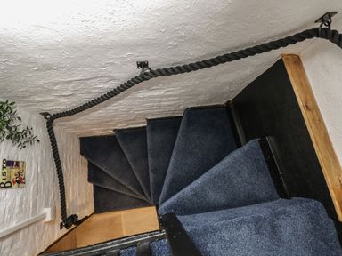 A narrow staircase with blue carpet and a black rope handrail attached to white textured walls at Avonmede in Tewkesbury