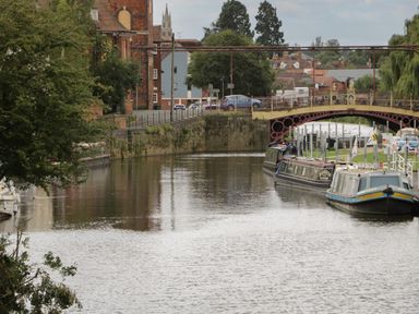 A river with boats docked near a bridge and buildings in the background at Avonmede in Tewkesbury