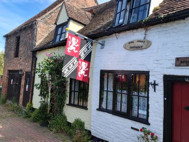 A view of King John's Cottages with flags and flowers in Tewkesbury