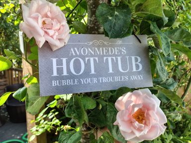 A sign indicating Avonmede's hot tub in a garden with roses in Tewkesbury