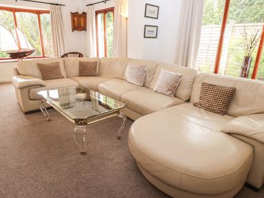 A living room with a large beige sectional sofa and a glass coffee table at Fir Trees in Bowness-On-Windermere