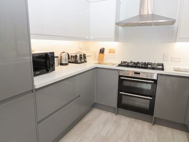 A kitchen with grey lower cabinets white upper cabinets a microwave kettle toaster knife block and stove at Fir Trees in Bowness-On-Windermere