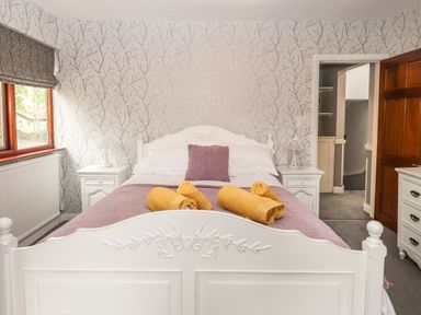 A bedroom with a white carved bed frame purple bedding and yellow towels on the bed at Fir Trees in Bowness-On-Windermere