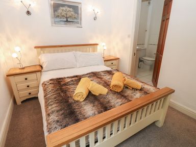 A bedroom with a bed with rolled towels on a fur blanket and bedside tables with lamps at Fir Trees in Bowness-On-Windermere