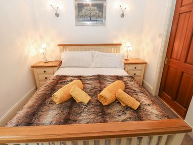 A bedroom with a bed with yellow towels on a fur blanket and wooden bedside tables at Fir Trees in Bowness-On-Windermere