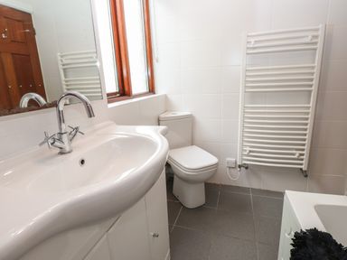 A bathroom with a sink, toilet, heated towel rail, window, and bathtub at Fir Trees in Bowness-On-Windermere