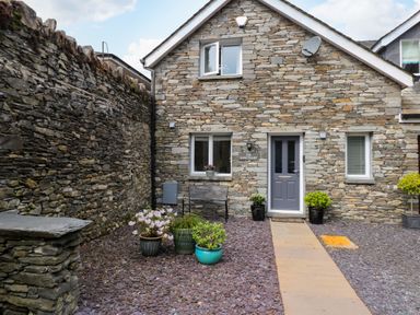 Stone house exterior with a pathway leading to a gray door and potted plants on stone ground at The Sanctuary in Windermere