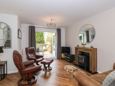 A living room with two brown leather chairs a small wooden mantel with a round mirror above a fireplace and a TV unit near a door leading to a patio at The Sanctuary in Windermere