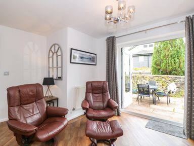 A sitting area with two brown leather chairs a table with a lamp a wall mirror and an open door leading to a patio with a table and chairs at The Sanctuary in Windermere