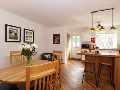 A kitchen and dining area with wooden table and chairs a kitchen island with stools and hanging lights at The Sanctuary in Windermere