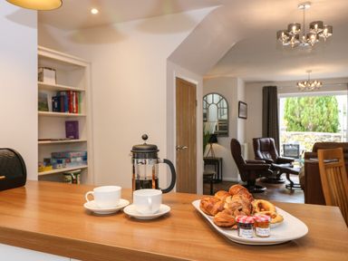 A kitchen counter with a French press coffee maker two white cups and saucers and a plate of pastries in an open plan living and dining area at The Sanctuary in Windermere