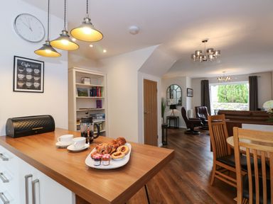 A kitchen counter with coffee cups and pastries leading to a living area with chairs and a sofa at The Sanctuary in Windermere