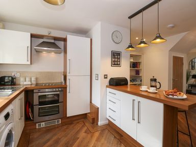 A kitchen with white cabinets wooden countertops an oven a stovetop a toaster a sink a washing machine and hanging pendant lights at The Sanctuary in Windermere