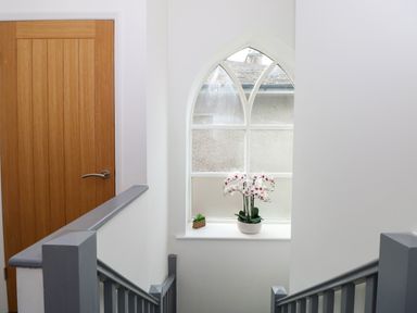 A stairway with gray railings a wooden door and a pointed arched window with plants on the sill at The Sanctuary in Windermere