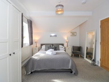 A bedroom with a bed gray bedding two nightstands with lamps a wardrobe a chair a large mirror and a wooden door at The Sanctuary in Windermere