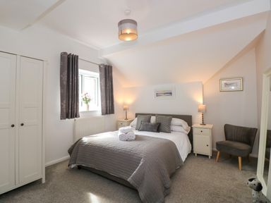 A bedroom with a bed and bedside tables with lamps a wardrobe a window with curtains and a chair at The Sanctuary in Windermere