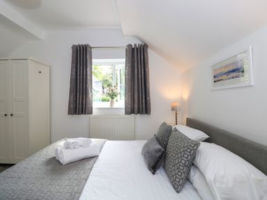 A bedroom with a bed made with white and gray linens two pillows rolled towels a lamp a window with gray curtains and a white wardrobe at The Sanctuary in Windermere