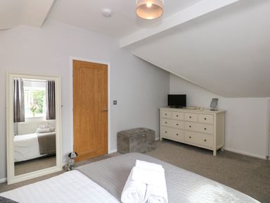 A bedroom with a bed, a full-length mirror, a wooden door, a dresser with a TV, and a gray cushioned storage bench at The Sanctuary in Windermere