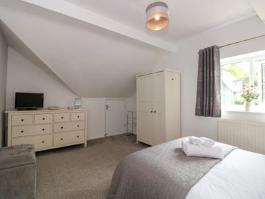 A bedroom with a bed towels on it a window with curtain a wardrobe a chest of drawers with a small tv and mirror at The Sanctuary in Windermere