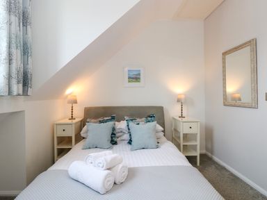 A bedroom with a bed with pillows and rolled towels on it two bedside tables with lamps a framed picture on the wall and a mirror at The Sanctuary in Windermere