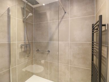 A tiled bathroom shower area with a glass partition a rainfall showerhead and a black towel radiator at The Sanctuary in Windermere