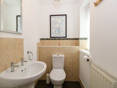 A bathroom with a toilet a sink a mirror a window and a framed map on the wall at The Sanctuary in Windermere