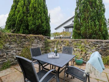 An outdoor patio area with a square table and four chairs next to a stone wall with small plants at The Sanctuary in Windermere