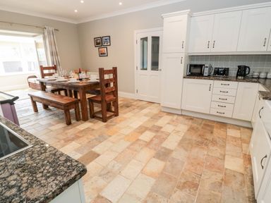 A kitchen with white cabinets wooden dining table and chairs next to a window at Deanrise in Shilbottle near Alnwick