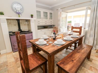 A dining area with wooden table set with dishes and wine inside a kitchen with an oven at Deanrise in Shilbottle near Alnwick