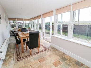 A dining area with a wooden table and black chairs next to windows and a door at Deanrise in Shilbottle near Alnwick