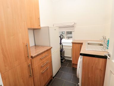 A utility room with wooden cabinets a white refrigerator a sink and a vacuum cleaner at Deanrise in Shilbottle near Alnwick