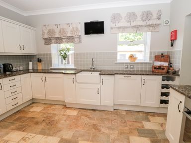 A kitchen with white cabinets granite countertops tiled floor two windows and a small wall-mounted television at Deanrise in Shilbottle near Alnwick