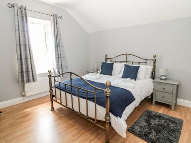A bedroom with a metal bed frame blue cushions on a bed bedside tables and grey curtains at Deanrise in Shilbottle near Alnwick