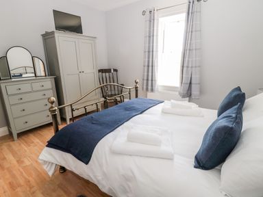 A bedroom with a bed a wardrobe a dresser with mirrors a wooden chair and a window with curtains at Deanrise in Shilbottle near Alnwick