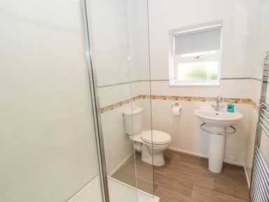 A bathroom with a shower enclosure a toilet and a sink with a window above at Deanrise in Shilbottle near Alnwick