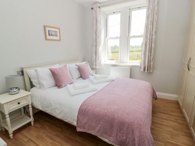 A bedroom with a double bed pink pillows and throw a bedside table lamp and wardrobe at Deanrise in Shilbottle near Alnwick