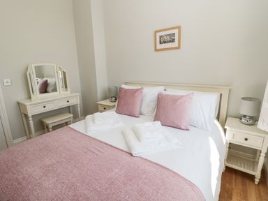 A bedroom with a double bed pink pillows pink throw white linens bedside tables with lamps and a dressing table at Deanrise Shilbottle near Alnwick
