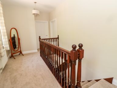 A hallway with a carpeted floor a wooden banister a standing mirror and two closed doors at Deanrise in Shilbottle near Alnwick