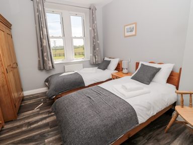 A bedroom with two single beds a wooden wardrobe and a window with curtains at Deanrise in Shilbottle near Alnwick