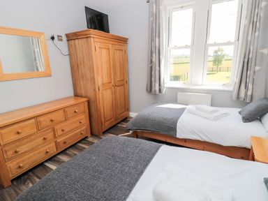 A bedroom with two single beds a wooden wardrobe a wooden dresser and a window with curtains at Deanrise in Shilbottle near Alnwick