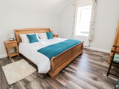 A bedroom with a wooden bed blue cushions a small rug and a window at Deanrise in Shilbottle near Alnwick