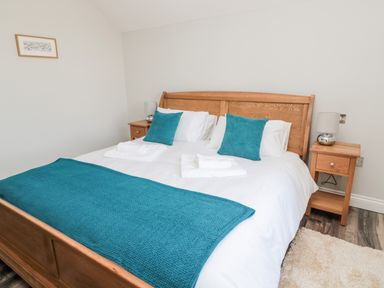 A bedroom with a wooden bed frame blue pillows blue blanket white bedding two bedside tables with lamps and a small framed picture on the wall at Deanrise in Shilbottle near Alnwick