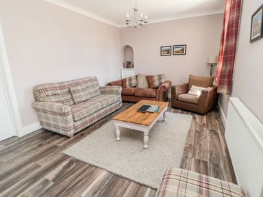 A living room with sofas a coffee table a rug and framed pictures on the wall at Deanrise in Shilbottle near Alnwick